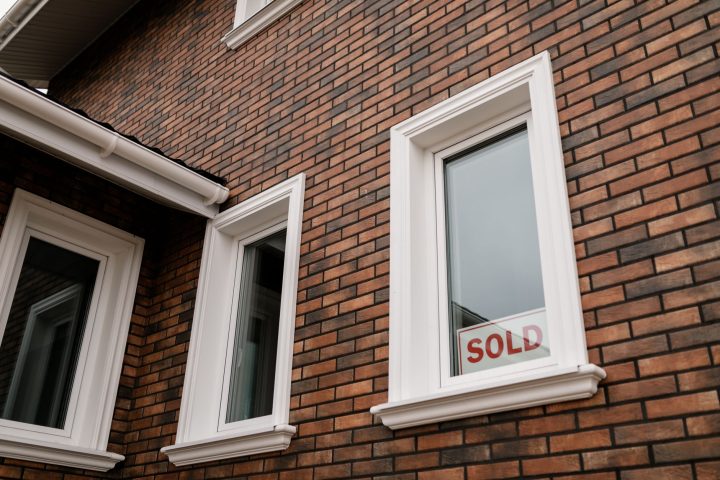 Close-up of a brick house with a 'Sold' sign in the window, showcasing real estate sales.